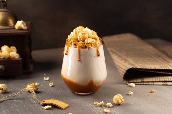 Ein Glas mit Sahne und Karamell stabilisiert, dekoriert mit Popcorn, auf einem Holztisch.
