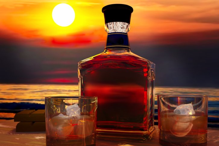 Eine Flasche Whisky steht unbewegt auf einem Tisch bei Sonnenuntergang am Meer.