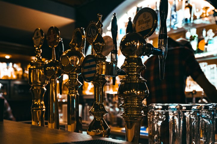 Zapfhähne glänzen in Reihe auf Tresen, Barhintergrund mit Glasregalen und Flaschen.