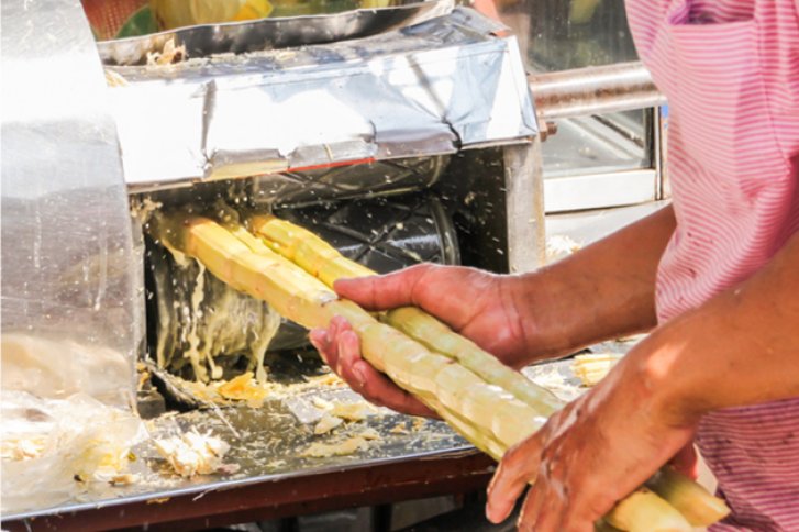 Zuckerrohr wird von einer Person durch eine Saftpresse geschoben, um Saft zu extrahieren.