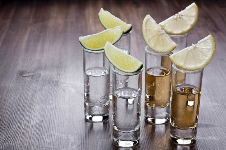 Fünf Shotgläser mit Limetten und Salz stehen auf einem Holztisch, gefüllt mit verschiedenen Spirituosen.