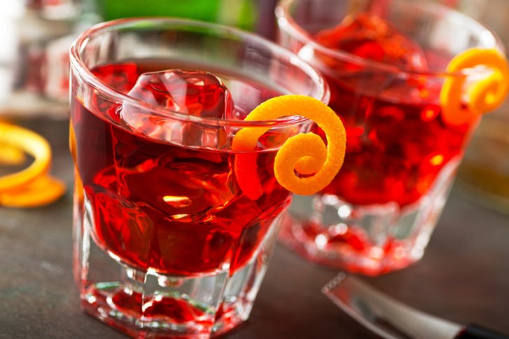 Zwei Drinks mit Eiswürfeln und Orangenschale stehen auf einem Tisch mit verschwommener Umgebung.