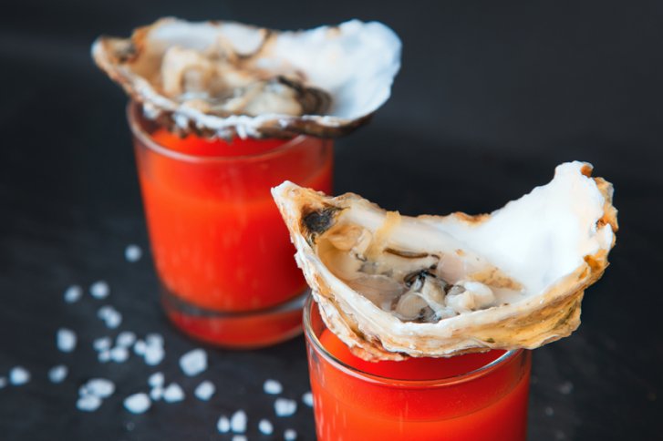 Austern liegen auf roten Cocktails in Gläsern auf schwarzem Hintergrund mit Salzstreuseln.