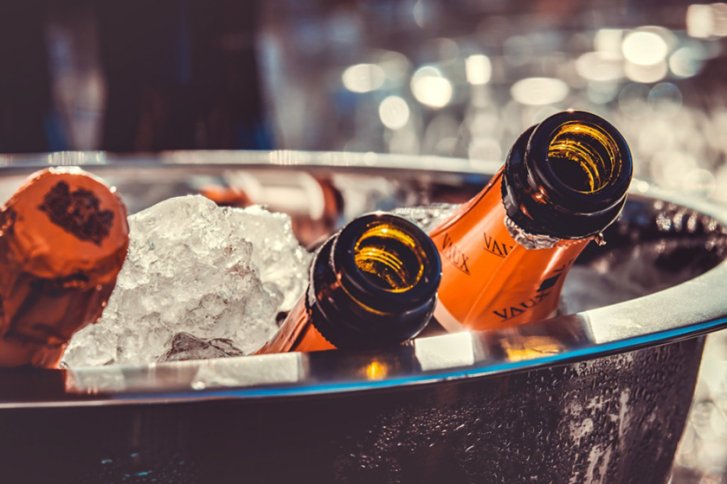 Champagnerflaschen stecken in einem Eiskübel, umgeben von verschwommenem, festlichem Hintergrund.