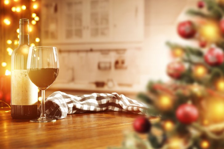 Weinflasche und Glas stehen auf Holztisch, umgeben von Weihnachtsdekoration und warmem Lichterglanz.