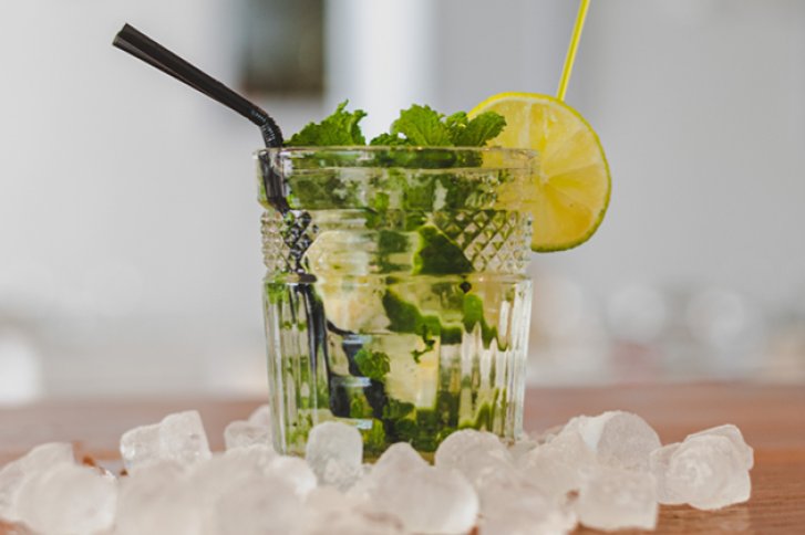 Ein Glas mit Mojito, dekoriert mit Limettenscheibe, steht auf einem Tisch voller Eiswürfel.