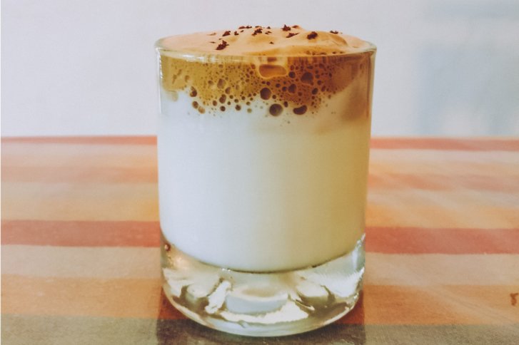 Glas mit Schichtgetränk, Schaum oben, steht auf gestreiften Tisch.