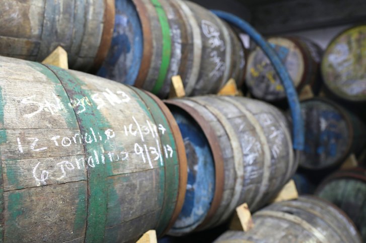 Holzfässer liegen gestapelt in einem Keller, mit Kreide beschriftet.