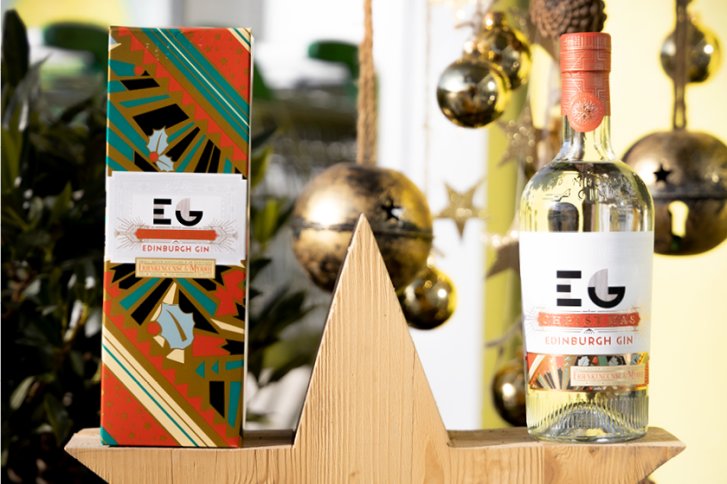 Flasche und Box Edinburgh Gin stehen auf Holzstern, dekoriert mit weihnachtlichen Ornamenten.