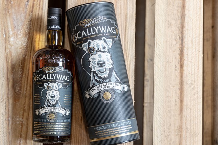 Flasche und Dose „Scallywag“ Whisky stehen auf Holzhintergrund, illustriertes Hundeetikett sichtbar.