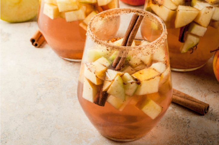 Ein Glas mit Apfelstücken und Zimtstangen steht auf hellem Untergrund, andere Gläser daneben.