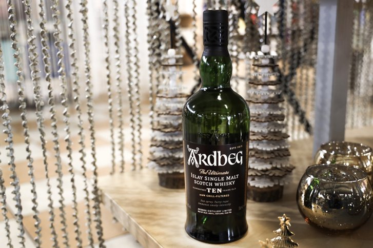 Eine Scotch-Whisky-Flasche steht auf einem Tisch, umgeben von dekorativen Weihnachtsbäumen und Kerzenhaltern.