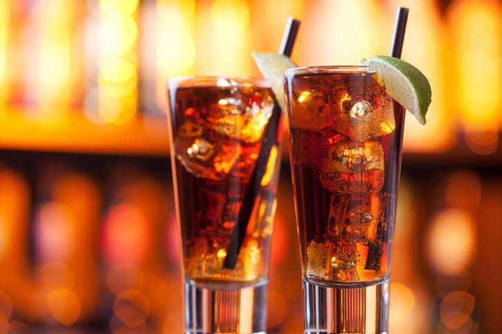 Zwei Longdrinks mit Limettenscheiben und Strohhalmen auf einer Bar, beleuchtet in warmem Licht.