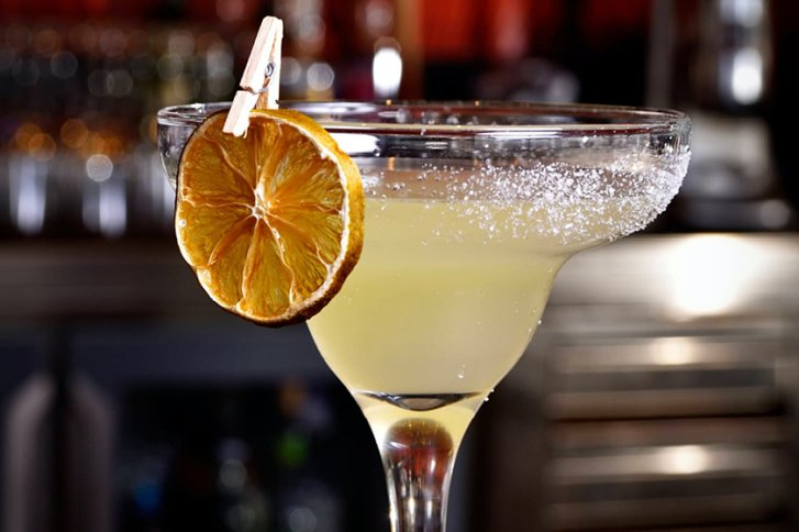 Ein Cocktailglas mit Zitrone am Rand steht vor verschwommenem Hintergrund in einer Bar.