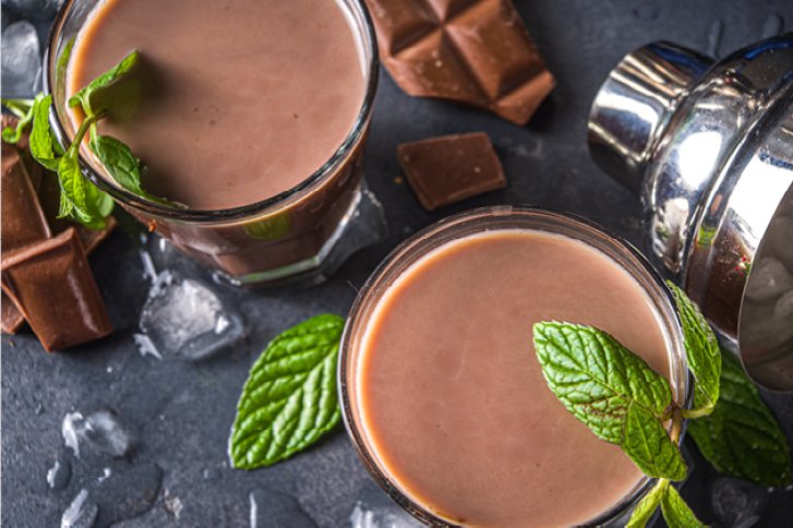 Zwei Schokoladencocktails stehen auf Eis, garniert mit Minzblättern; daneben Schokostückchen und Cocktailshaker.