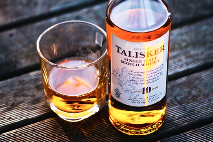 Flasche Talisker Whisky steht neben gefülltem Glas auf einem Holztisch in der Sonne.