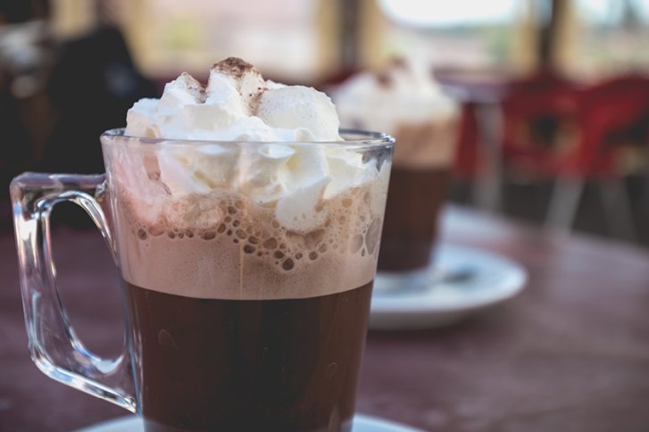 Glas mit Sahne auf Kaffee, stehend auf einem Tisch mit unscharfem Hintergrund in einem Café.