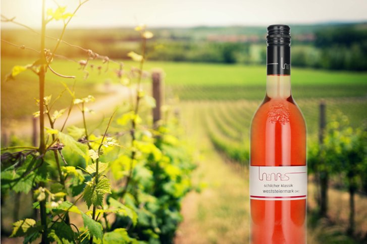 Eine Flasche Roséwein steht im Vordergrund eines sonnigen Weinbergs mit grünen Reben.