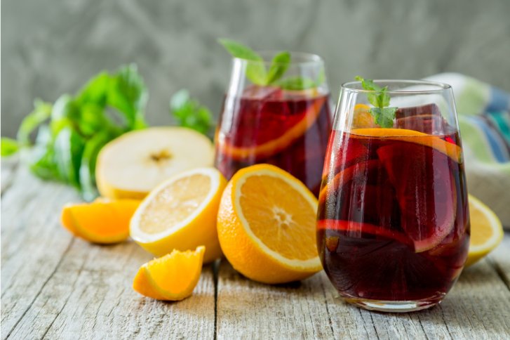 Zwei Gläser rote Sangria, geschmückt mit Orangen und Minze, stehen auf einem Holztisch.
