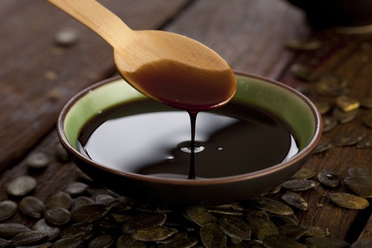 Ein Holzlöffel träufelt dunkles Öl in eine Schale, umgeben von Kürbiskernen.