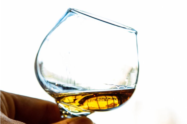 Ein Cognacglas mit goldenem Getränk wird gegen hellen Hintergrund in der Hand gehalten.