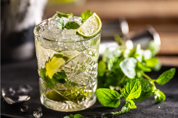 Ein Glas mit Mojito; gefüllt mit Eis, Limetten und Minze; auf Holzuntergrund.