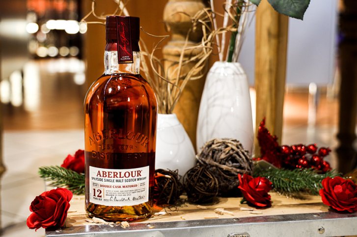 Flasche Aberlour Whisky steht dekoriert mit roten Rosen, Tannenzweigen und Holzelementen auf Holztisch.