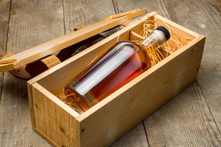 Flasche Whisky liegt in Holzkiste mit Stroh auf Holzfußboden.