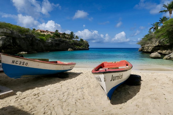 Zwei Boote liegen auf einem sandigen Strand vor einer malerischen, türkisfarbenen Bucht.