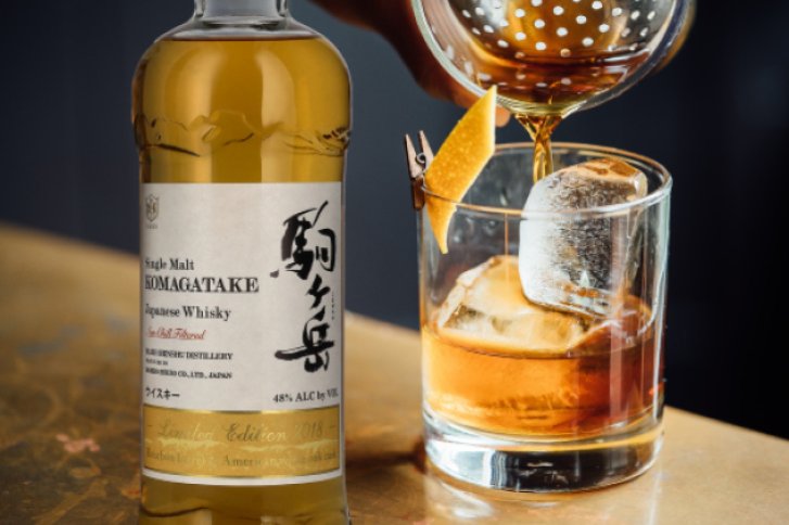 Eine Whiskyflasche steht neben einem Glas, in das ein Getränk eingeschenkt wird.