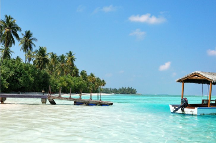Holzhütte steht still im klaren, türkisfarbenen Wasser neben Palmen und einem Steg.