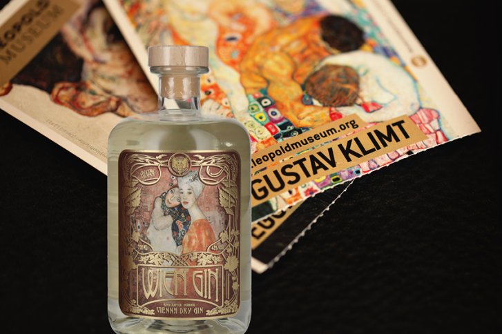 Gin-Flasche mit kunstvollem Etikett vor klimt-inspirierter Kunst, auf dunklem Hintergrund.