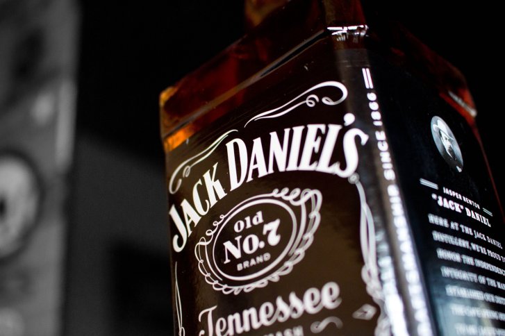 Flasche zeigt Etikett von Jack Daniel's Whiskey, schräg fotografiert, vor dunklem Hintergrund.