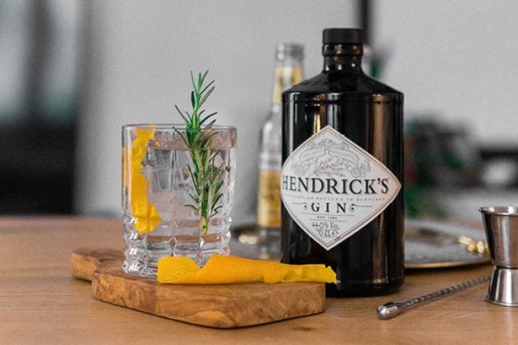 Ein schwarzer Hendrick’s Ginflasche steht neben einem Cocktailglas mit Zitrone und Rosmarin.
