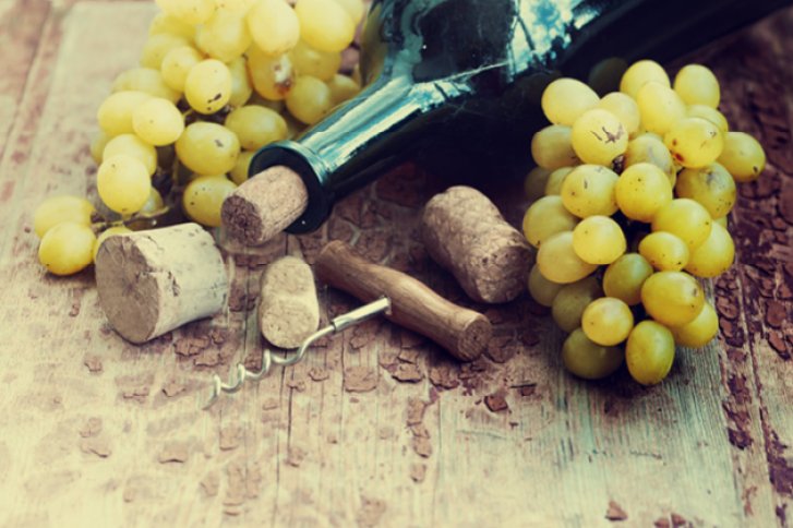 Weinflasche liegt auf Holztisch, umgeben von Weintrauben, Korken und Korkenzieher.