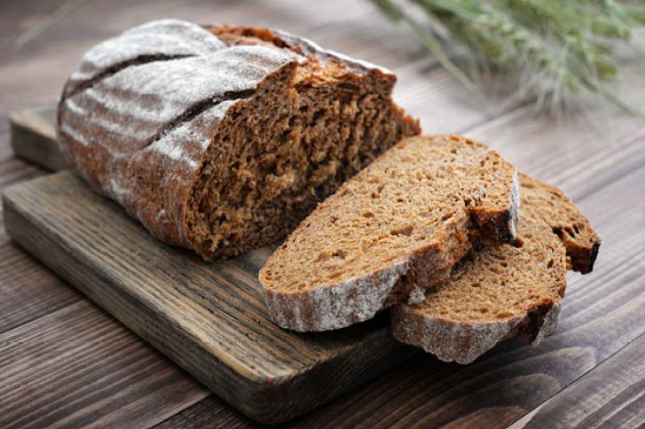 Ein dunkles Brotlaib aufgeschnitten auf einem rustikalen Holzbrett in hölzerner Umgebung.