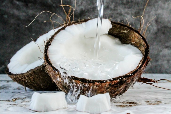 Halbe Kokosnuss füllt sich mit Wasser, steht auf rustikalem Tisch vor grauem Hintergrund.