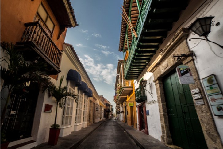 Straße erstreckt sich zwischen farbenfrohen Gebäuden, einige mit Balkonen, unter einem klaren Himmel.