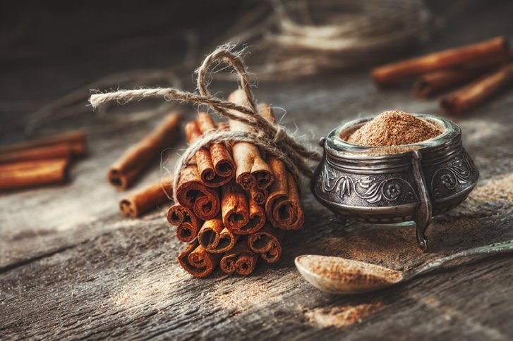 Zimtstangen liegen gebündelt auf Holztisch, daneben Schale und Löffel mit Zimtpulver.