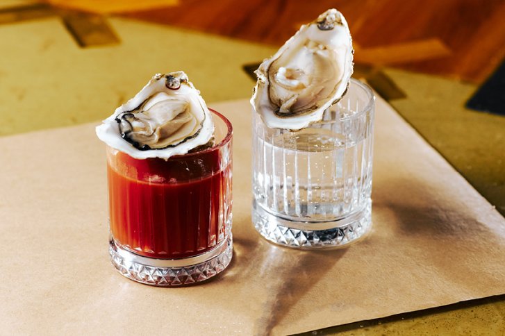 Zwei Gläser gefüllt mit roten und klaren Getränken, jeweils mit einer Auster garniert.