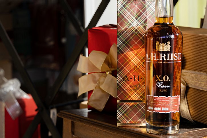 Flasche Rum steht auf Holztisch, umgeben von Geschenkboxen mit Schleifen.