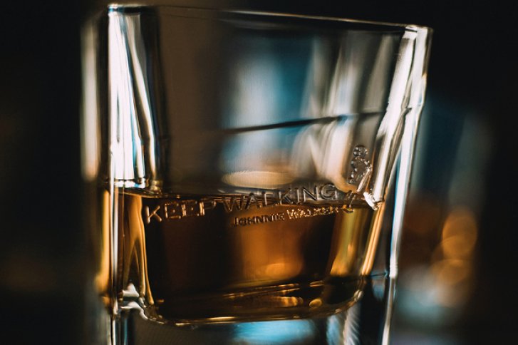 Ein Glas mit Whisky, halb gefüllt, steht in gedämpfter, dunkler Bar-Atmosphäre.