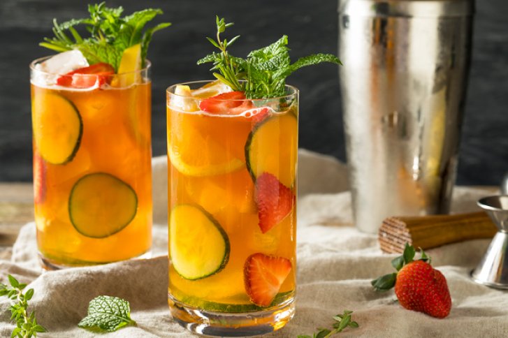 Zwei gefüllte Gläser mit Orangencocktail, dekoriert mit Gurken, Erdbeeren, Minze, stehen auf Stofftuch.