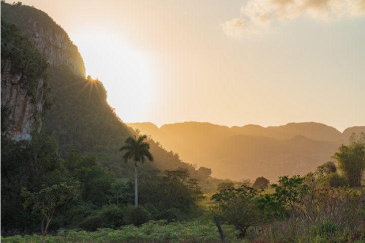 Felsformationen leuchten im Sonnenaufgang, umgeben von üppiger Vegetation in bergiger Landschaft.