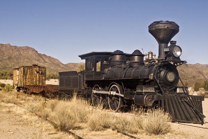 Alte Dampflok steht still in trockener, wüstenartiger Landschaft mit Bergen im Hintergrund.