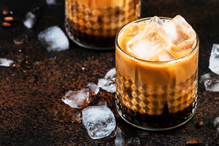 Zwei mit Eiswürfeln gefüllte Gläser Kaffee stehen auf einem dunklen, mit Eiswürfeln bedeckten Untergrund.