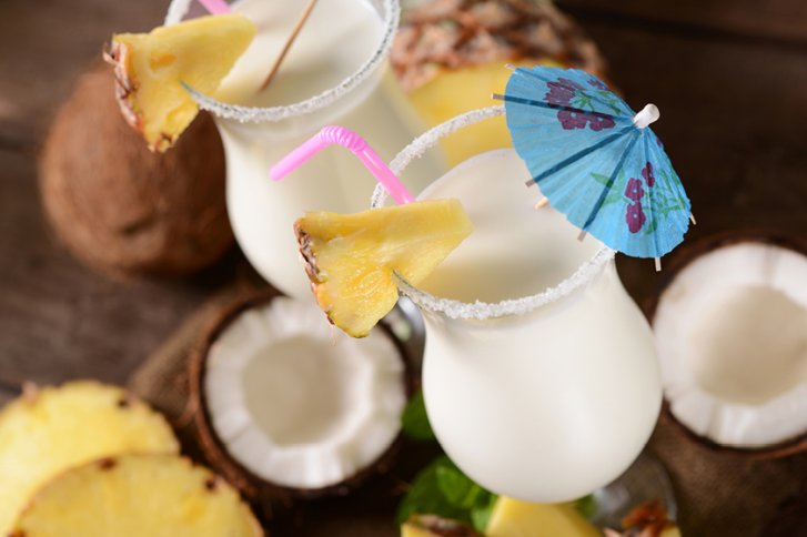 Zwei Pina Colada-Cocktails mit Ananas und Schirmchen auf Holztisch mit Kokosnüssen.