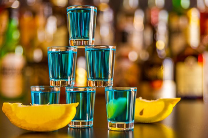 Blau gefüllte Shotgläser stapeln sich auf Bar, mit Zitronenscheiben dekoriert im Vordergrund.