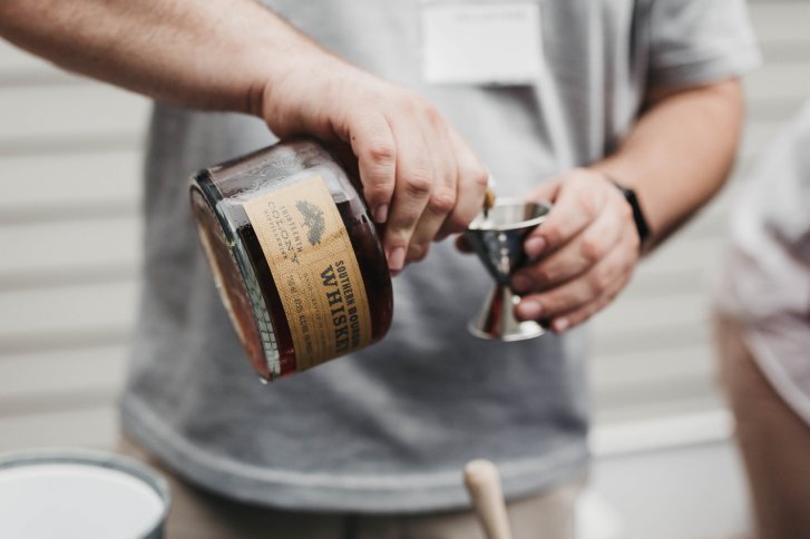 Mann gießt Whiskey aus Flasche in Messbecher, im Freien bei hellen Lichtverhältnissen.