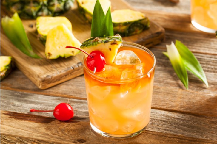 Ein Glas Cocktail mit Eis und Fruchtscheiben steht auf einem Holztisch.